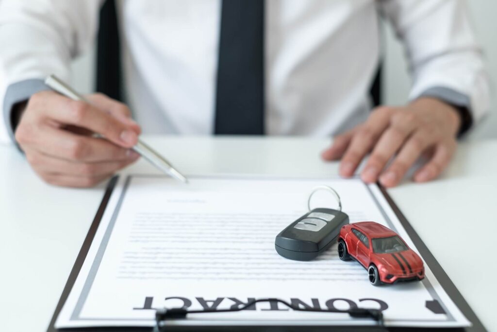 contratto di noleggio appoggiato sulla scrivania con una chiave e un modellino di un'auto rossa e un uomo che ha in mano una penna per firmare