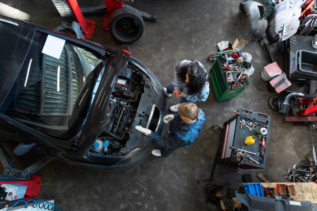 Meccanico controlla il motore di un’auto in officina spiegando il problema a un cliente.