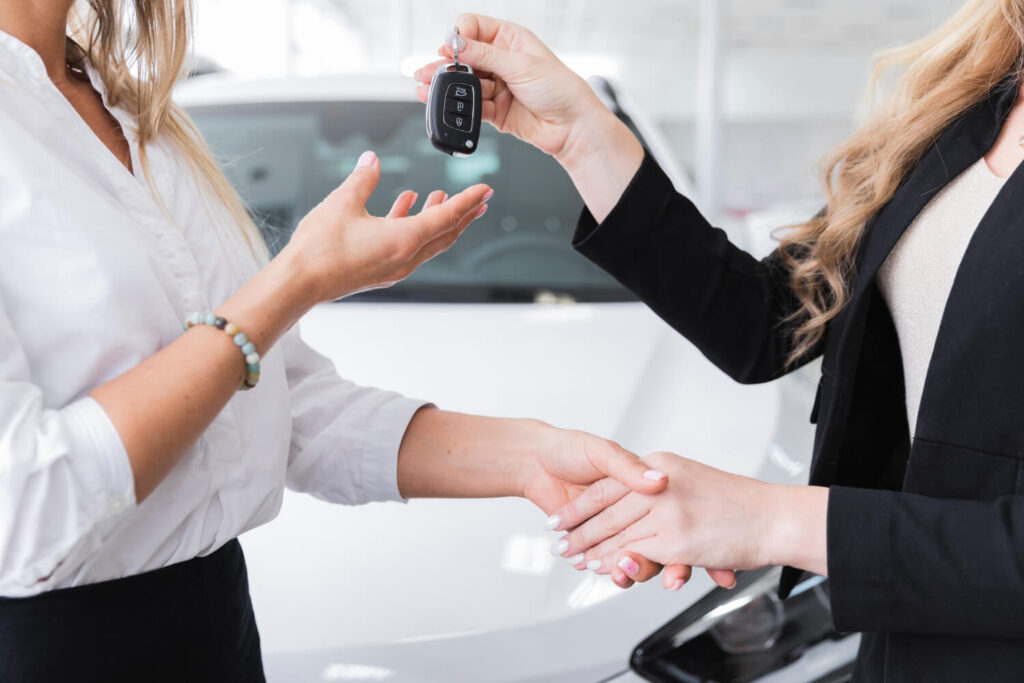 Due donne si stringono la mano mentre si scambiano una chiave dell'auto per un servizio di noleggio.