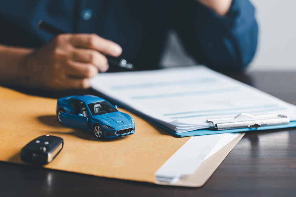 Rinnovo contratto di noleggio auto: persona valuta opzioni con documenti, chiavi e modellino di auto sul tavolo.
