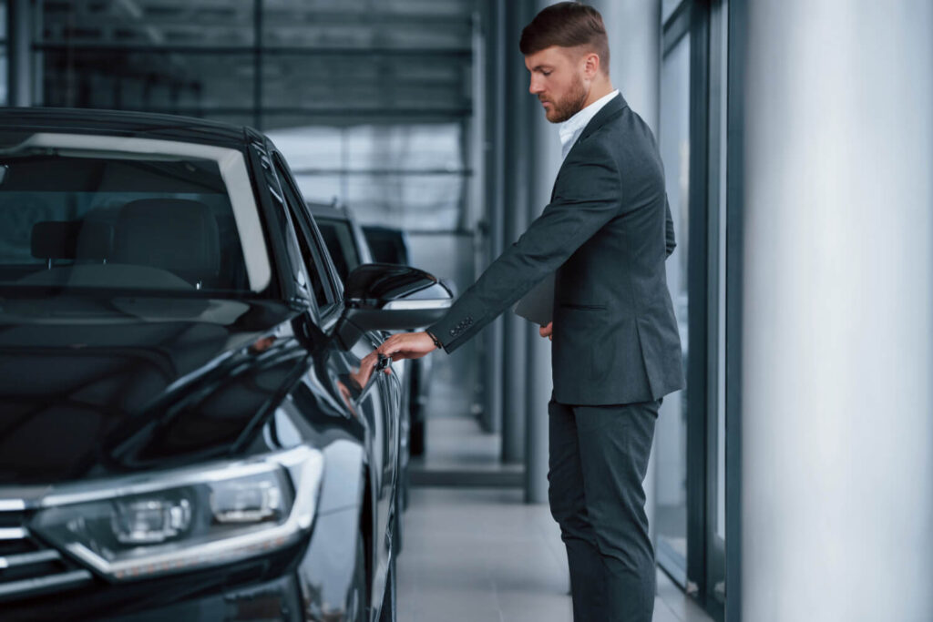 Uomo in abito elegante apre la portiera di un’auto nera in una concessionaria, concetto di scelta del veicolo per il noleggio a lungo termine o acquisto aziendale.
