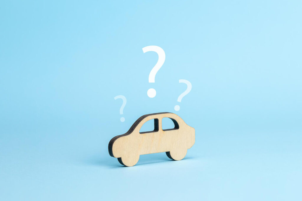 Sagoma in legno di un'auto con punti interrogativi su sfondo azzurro, simbolo del dubbio tra noleggiare o acquistare un'auto.