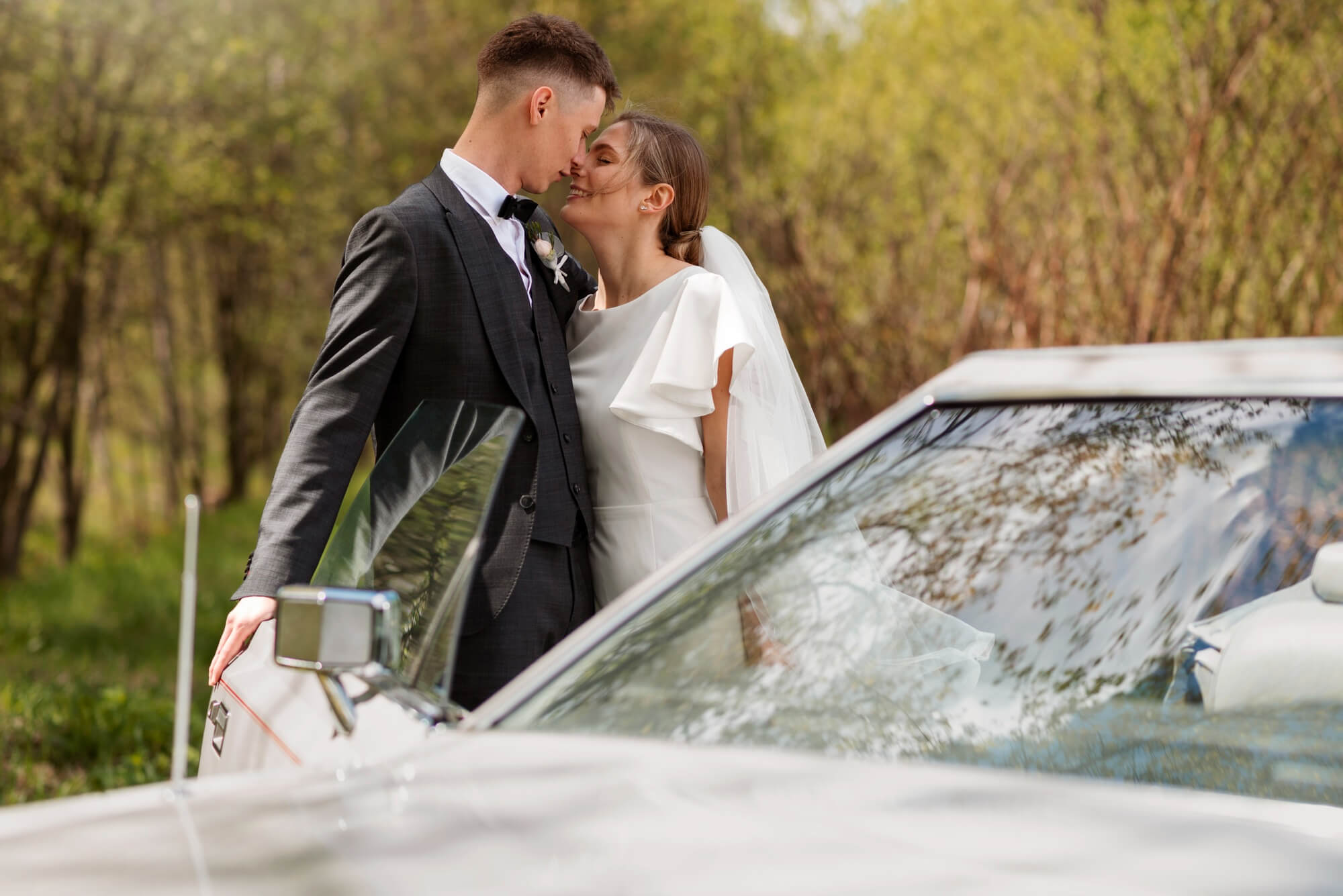 La sposa e lo sposo si scambiano un bacio affettuoso accanto a un'auto elegante