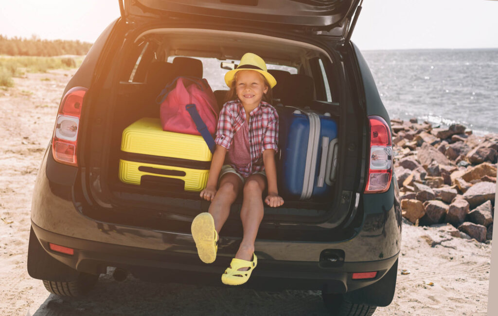 Bambina nel bagagliaio di un'auto a noleggio, con le valigie, sorridente e pronta per iniziare le vacanze