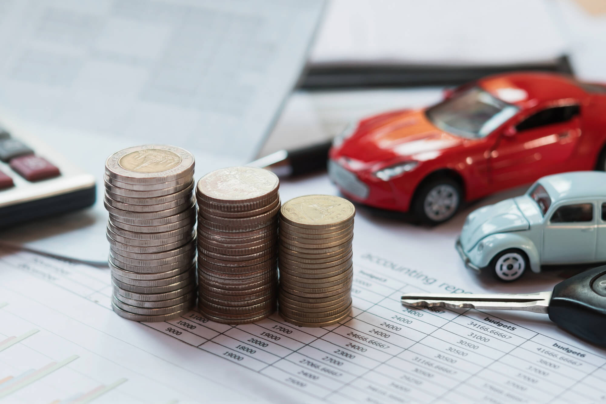 Due auto giocattolo e chiavi accanto a pile di monete