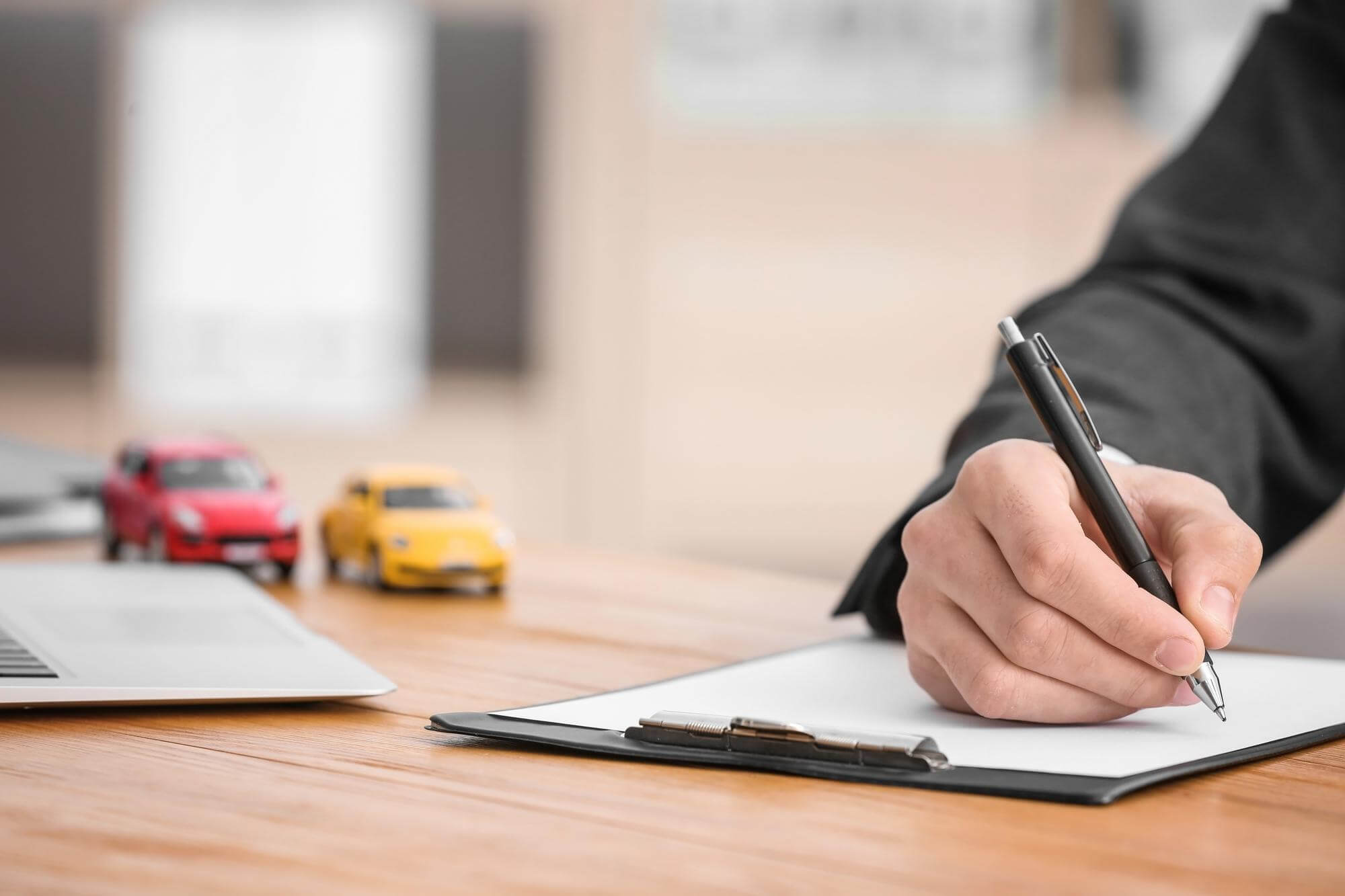 Un uomo scrive con una penna, mentre due auto giocattolo si vedono sullo sfondo